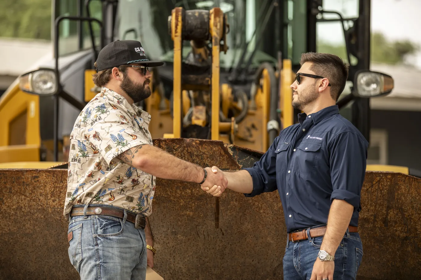 Two operators closing a deal with a handshake in front of a raised loader bucket