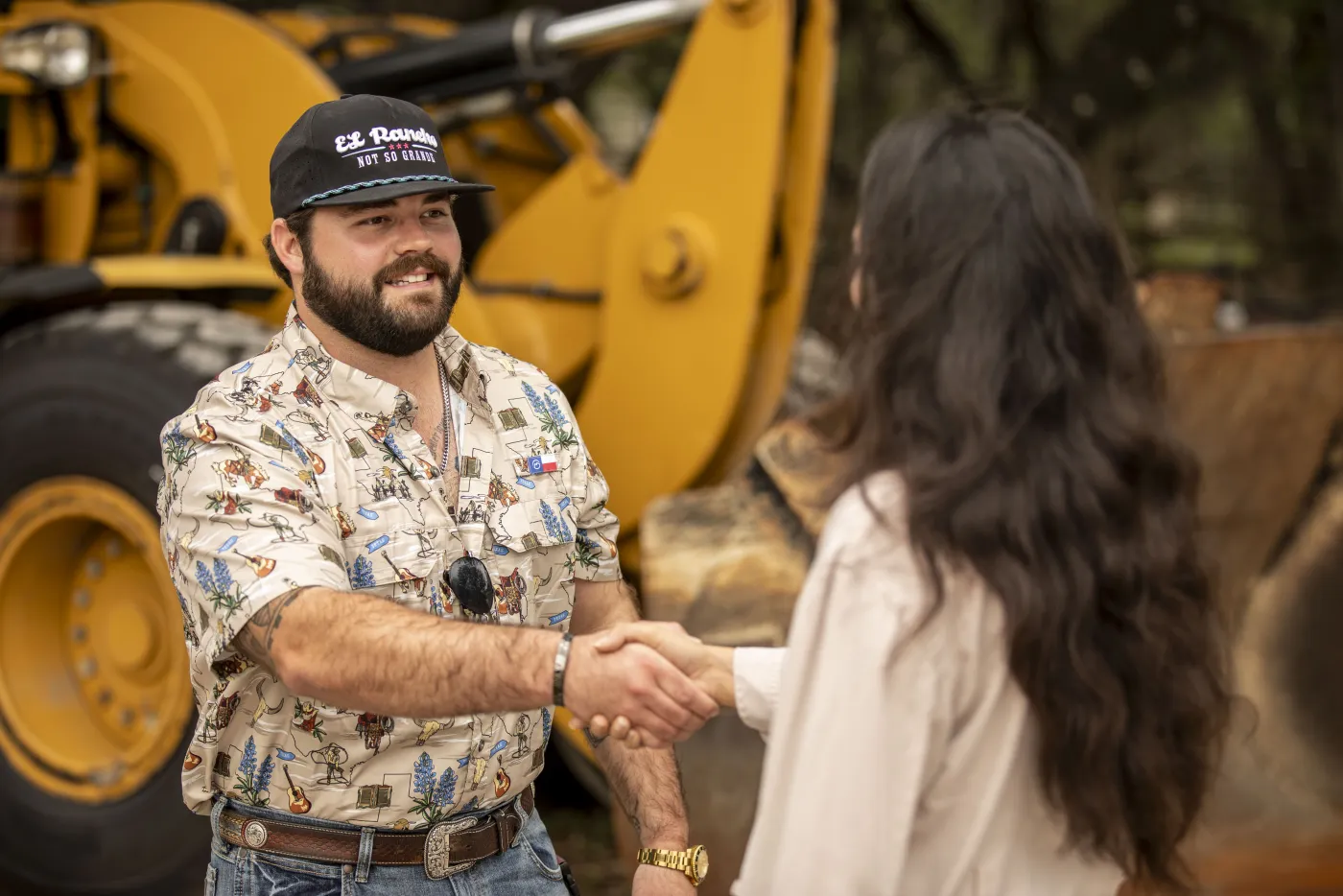A man and a woman shaking hands on a deal in front of a wheel loader