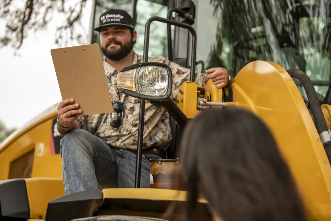 Tex rep with a clipboard talking through a wheel loader